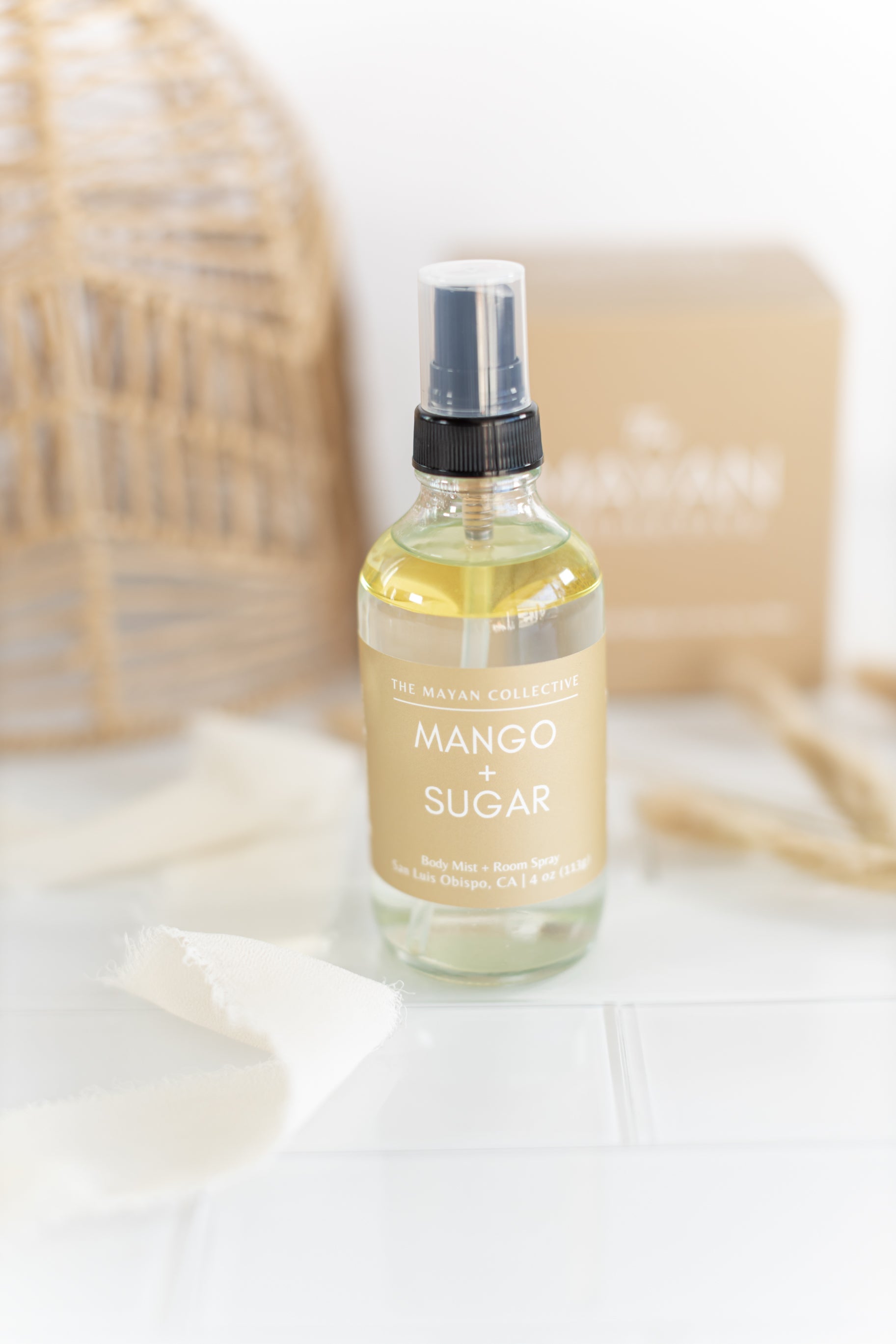 Mango Sugar body spray bottle on a white surface with a blurred background