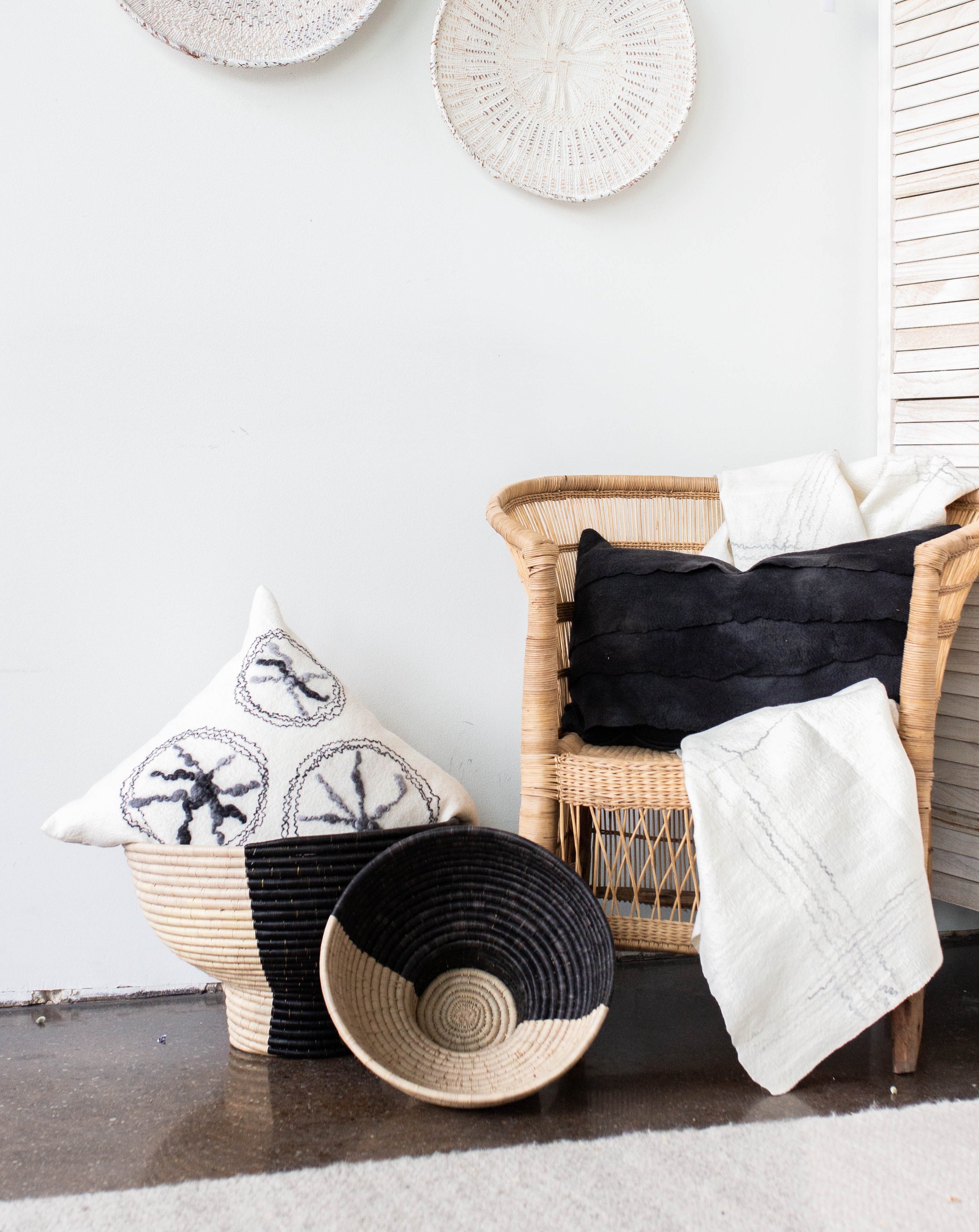 Wicker baskets with decorative pillows and a blanket against a white wall.
