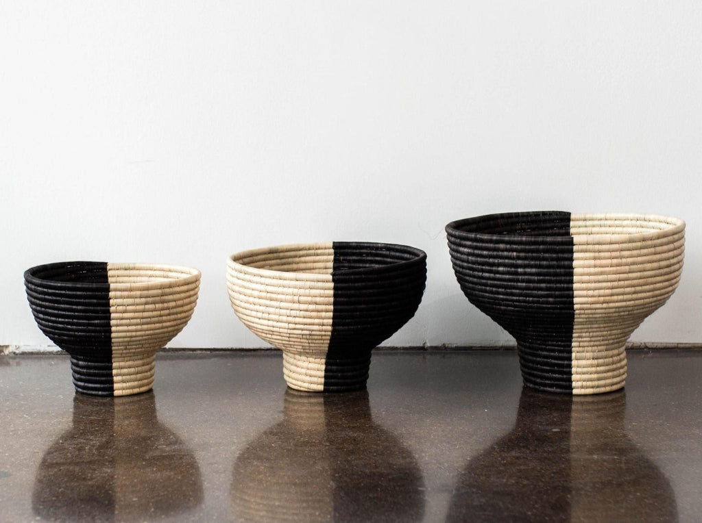Three black and beige woven baskets on a reflective surface with a white background