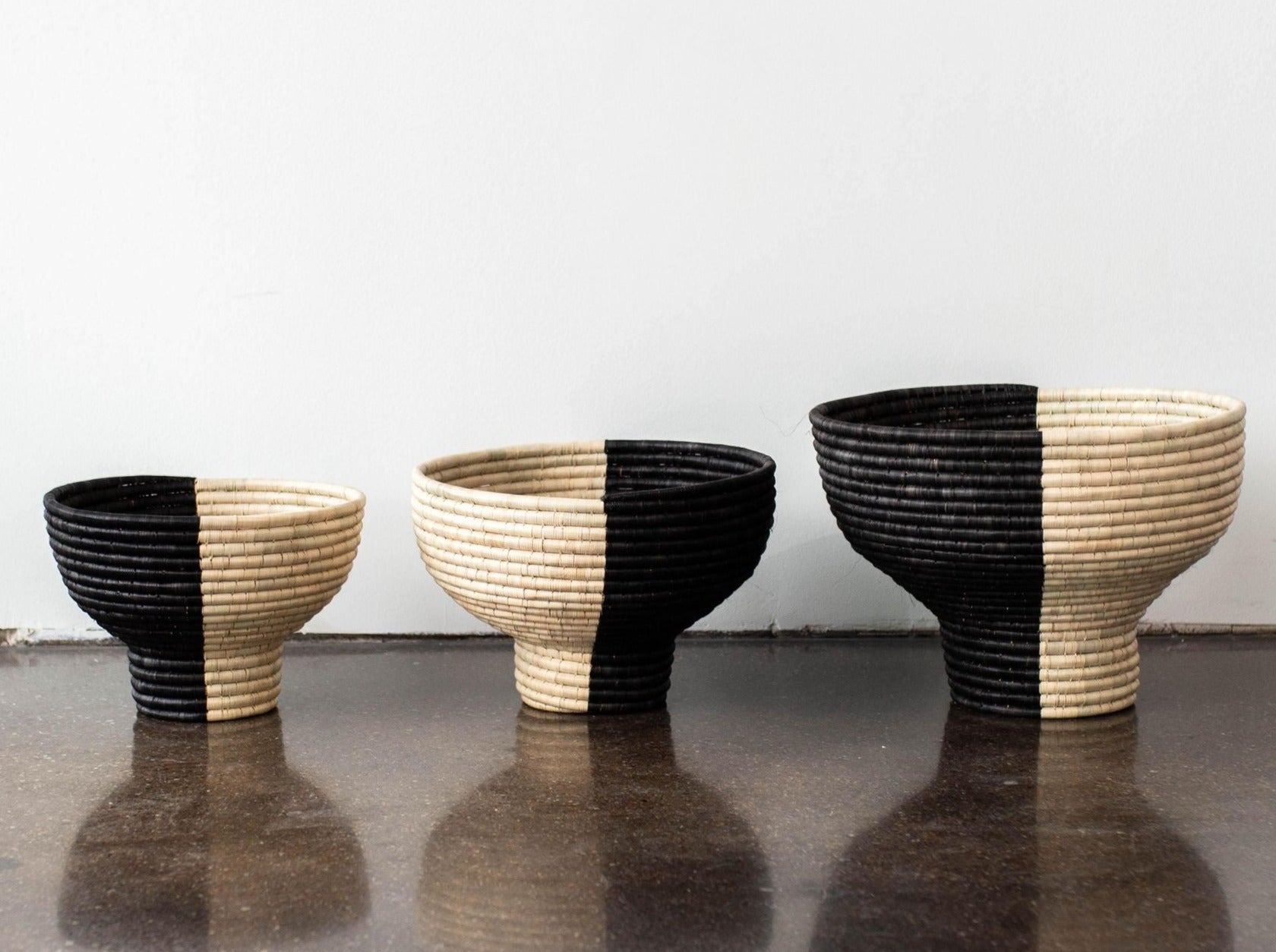 Three black and beige woven baskets on a reflective surface with a white background